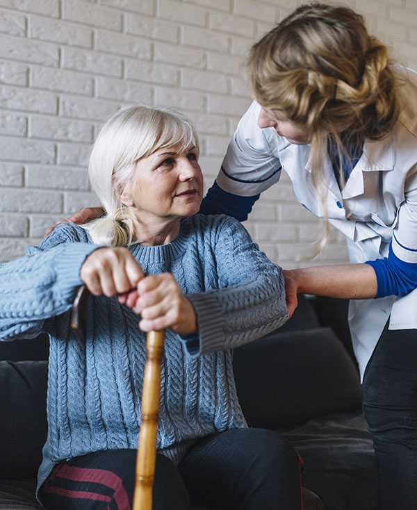 Caregiver helping client with cane get to her feet.